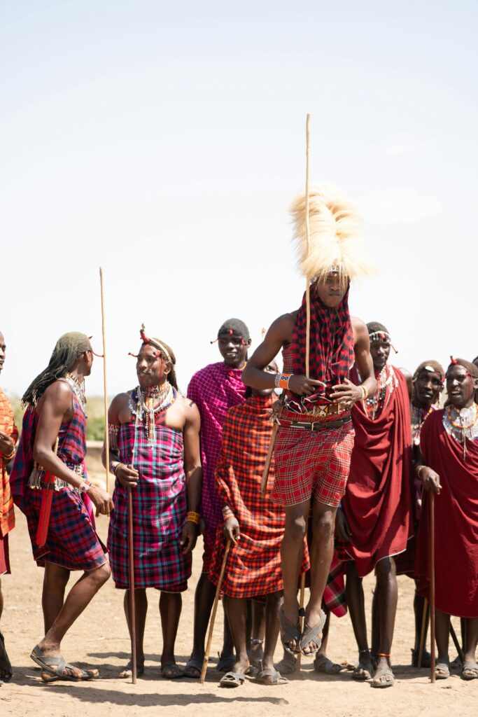 A group of Maasai tribesmen in colorful attire perform a traditional jumping dance outdoors in Kenya.